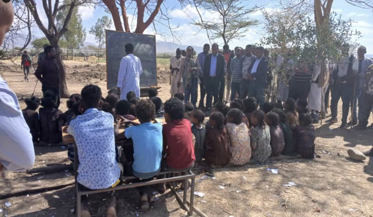 Children attending an outdoor classroom under trees in rural Tigray, taught on a makeshift chalkboard